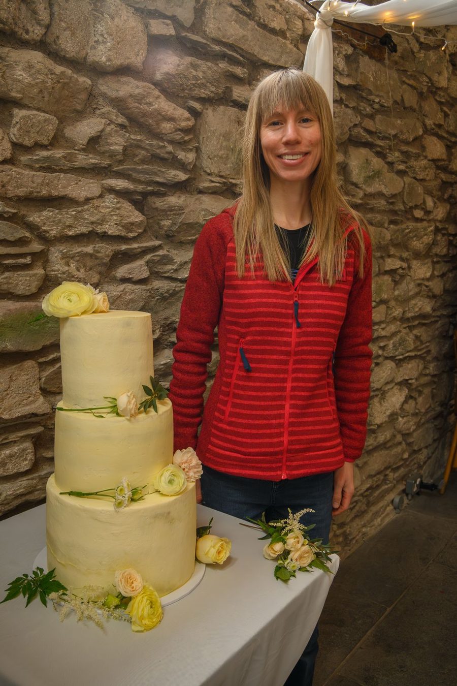 Holly standing beside a three tier wedding cake decorated with fresh flowers